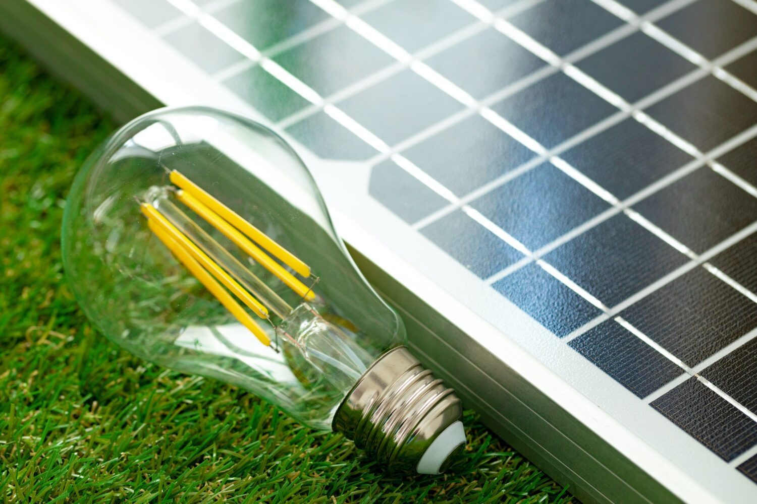 Close-up of a light bulb next to a solar panel on green grass