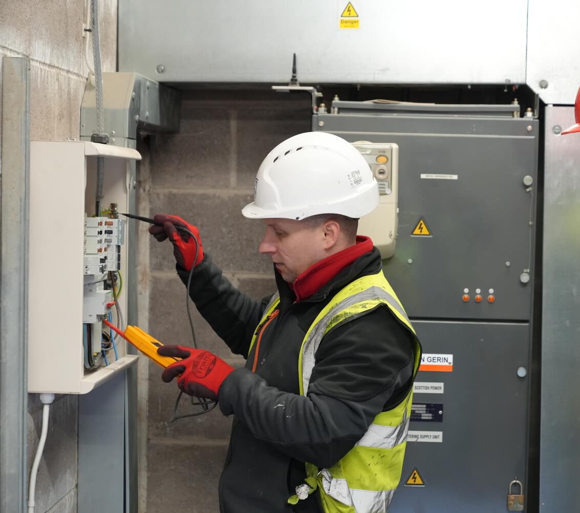 Electrician wearing a hard hat and safety vest working on a commercial electrical panel