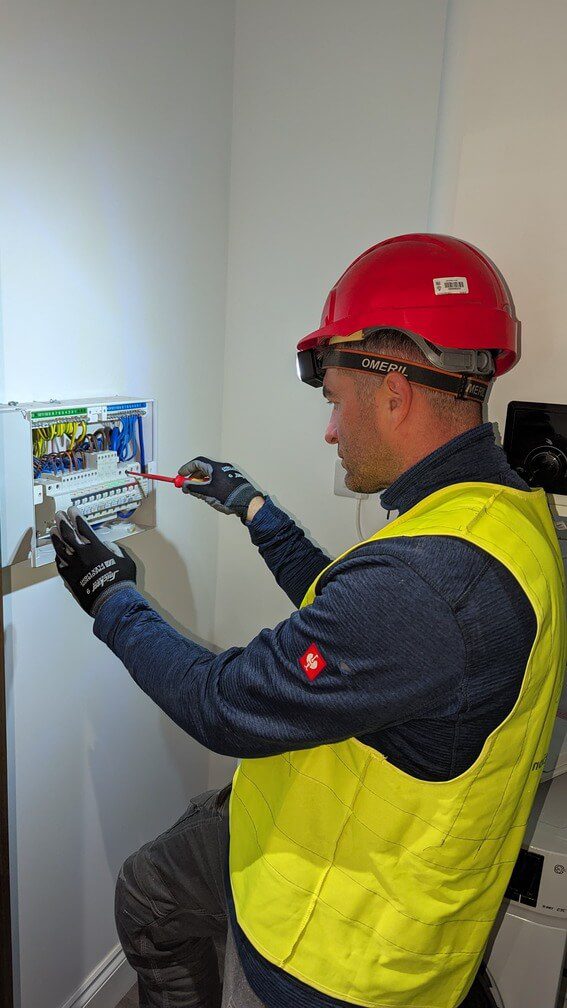 Electrician wearing a red hard hat and yellow safety vest working on an electrical panel